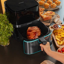 Cargar imagen en el visor de la galería, Freidora de aire Cecofry Full Inox 5500 Pro con su cesta extraída, revelando un trozo de carne perfectamente cocinado en su interior, rodeado de otros alimentos en la encimera de la cocina.
