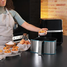 Cargar imagen en el visor de la galería, Una persona colocando un muffin en la cesta extraída de la freidora de aire Cecofry Full Inox 5500 Pro, con ingredientes para hornear en la encimera.
